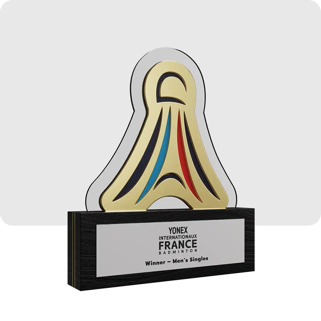 Trophée personnalisé de couleur doré, blanc, bleu, rouge et noir. La partie supérieur représente un volant de badminton posé sur un socle. 
