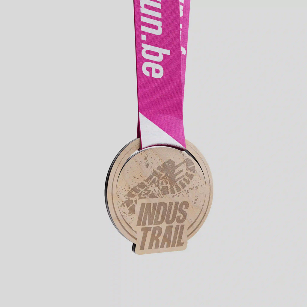 Médaille en bois Indus Trail avec empreinte de semelle gravée et ruban rose vif.