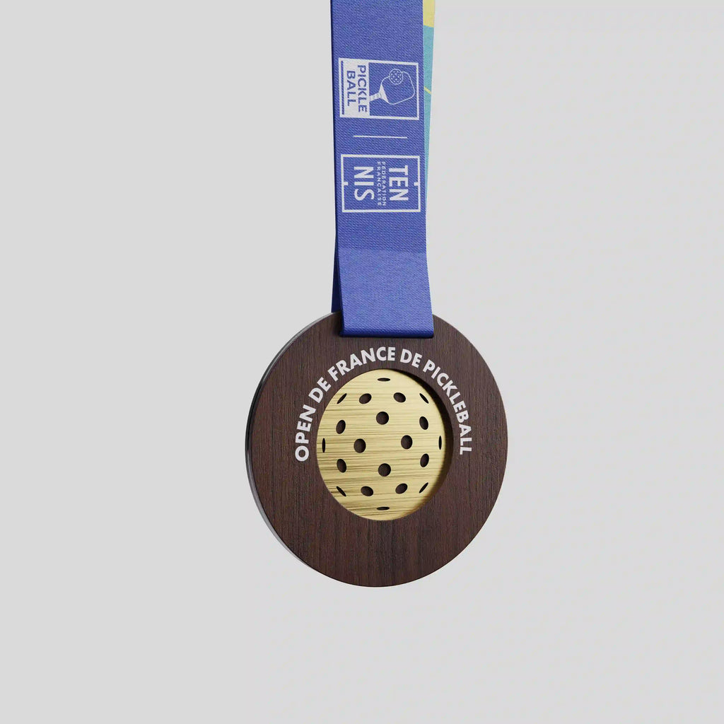 Médaille en bois foncé avec balle ajourée dorée pour l’Open de France de Pickleball.